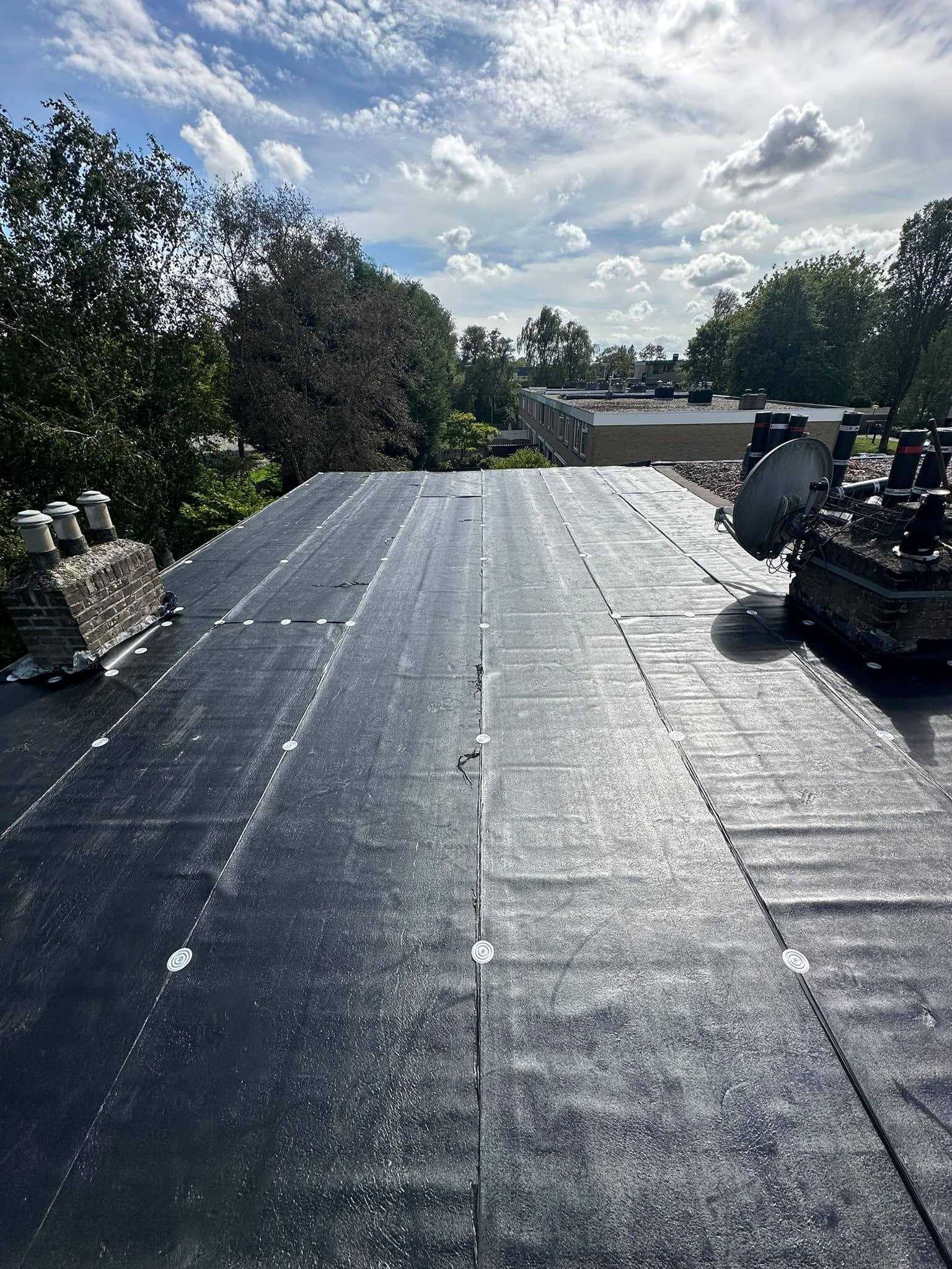 Nieuwe bitumen dakbedekking op een plat dak onder een wolkenlucht